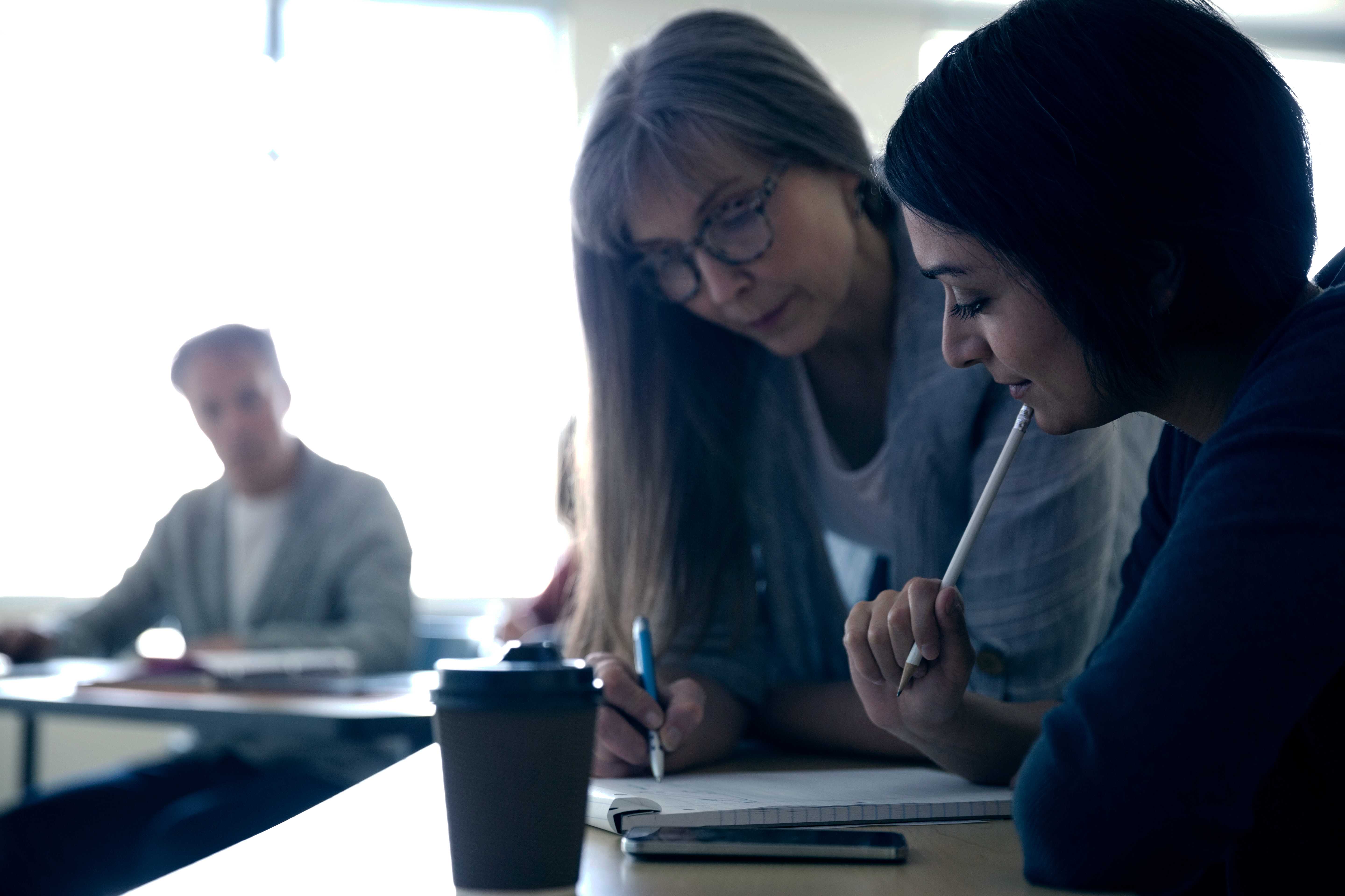 Two women looking at a notepad while holding pencils.